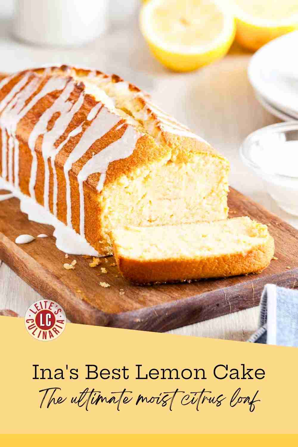 A golden lemon pound cake with white icing drizzle on a rustic wooden board with fresh lemons.