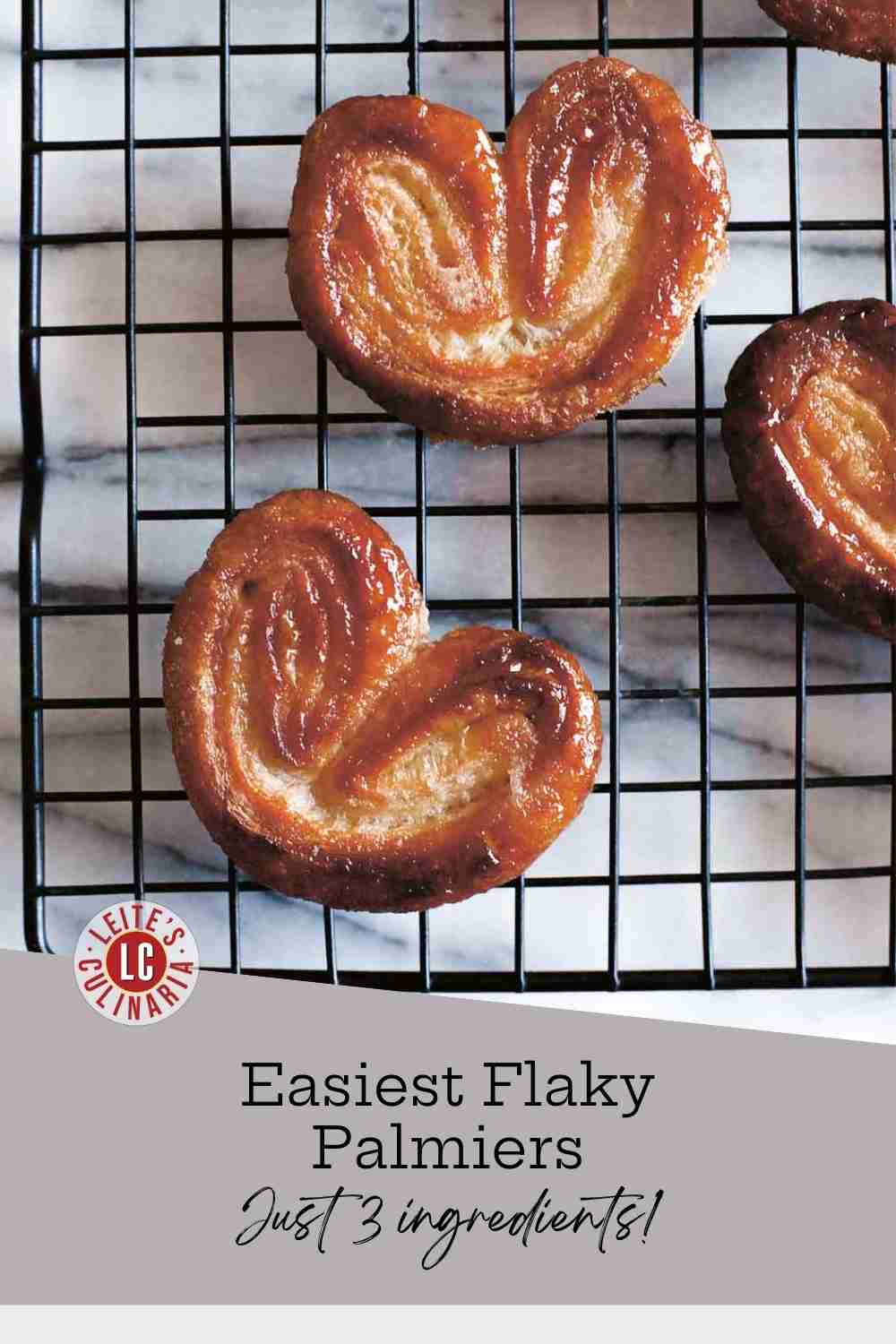 Three richly caramelized, heart-shaped palmiers, or elephant ears, resting on a black wire cooling rack on a marble surface.