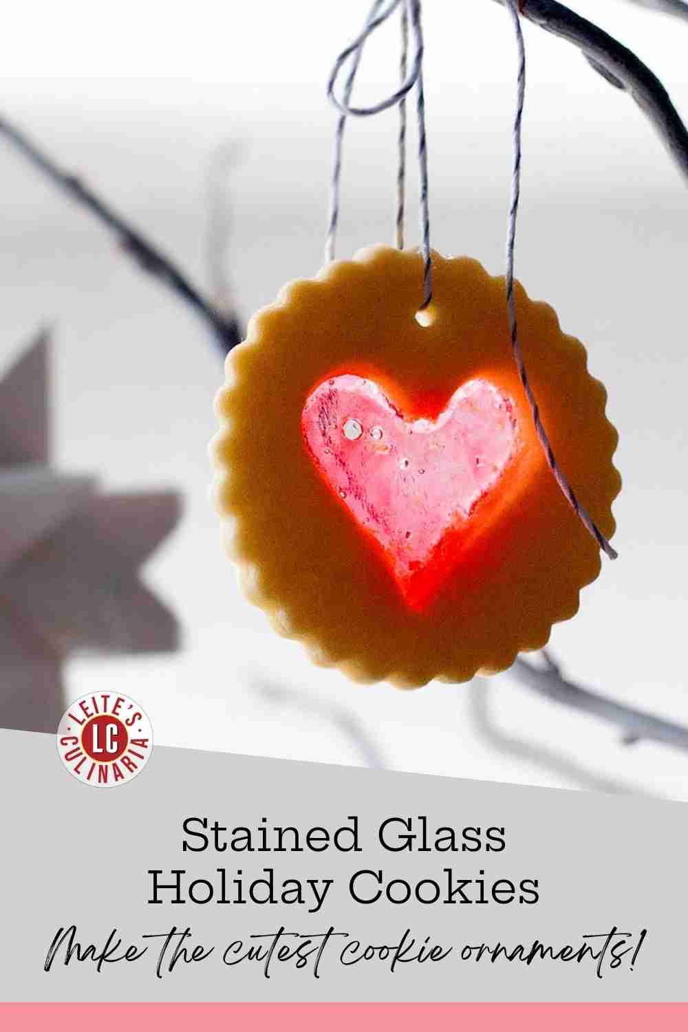 Scalloped sugar cookie with a translucent red hard candy heart center, tied with baker’s twine and hung on a bare branch.