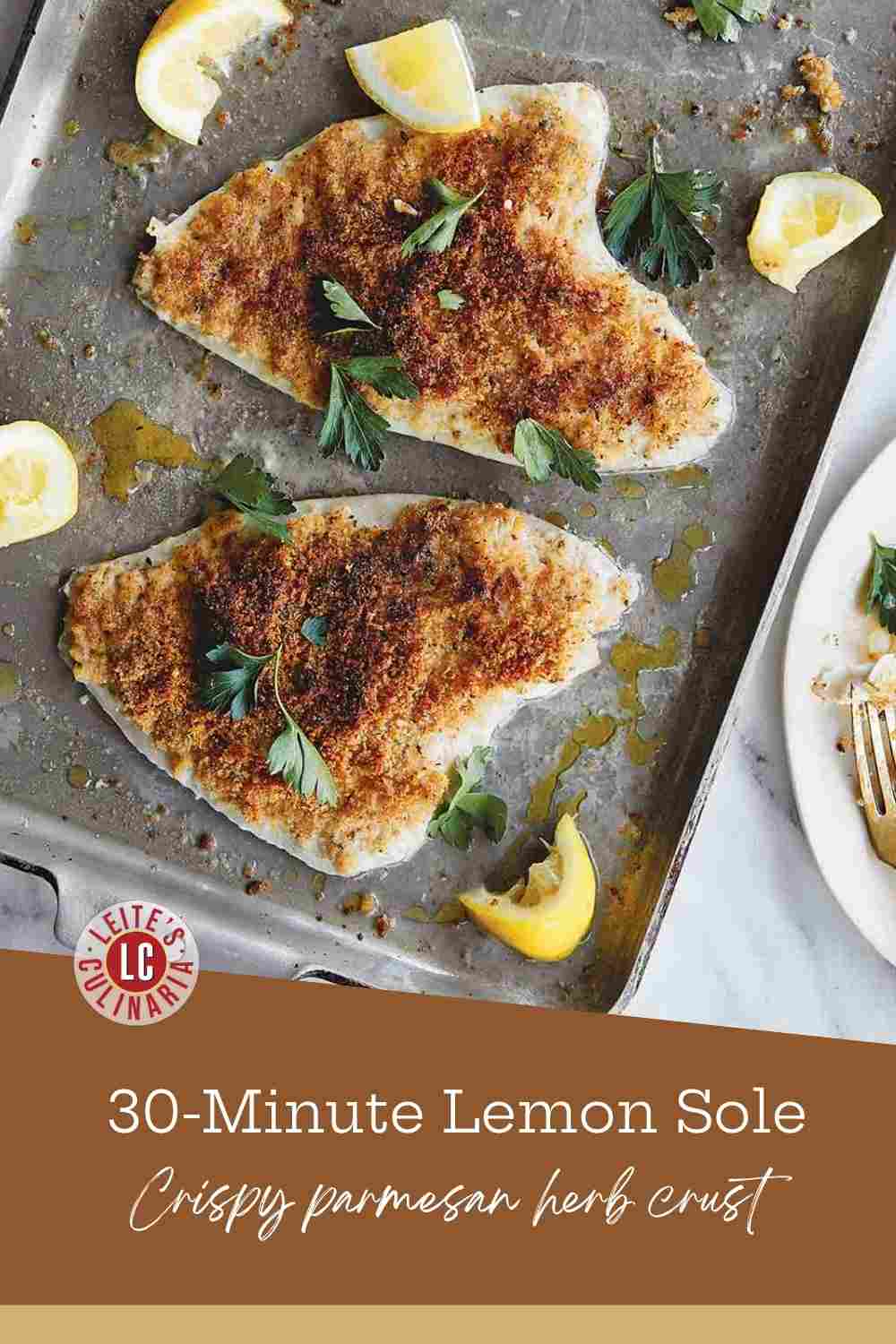 Two golden-brown breaded fish fillets on a rimmed baking sheet with lemon wedges and fresh parsley.
