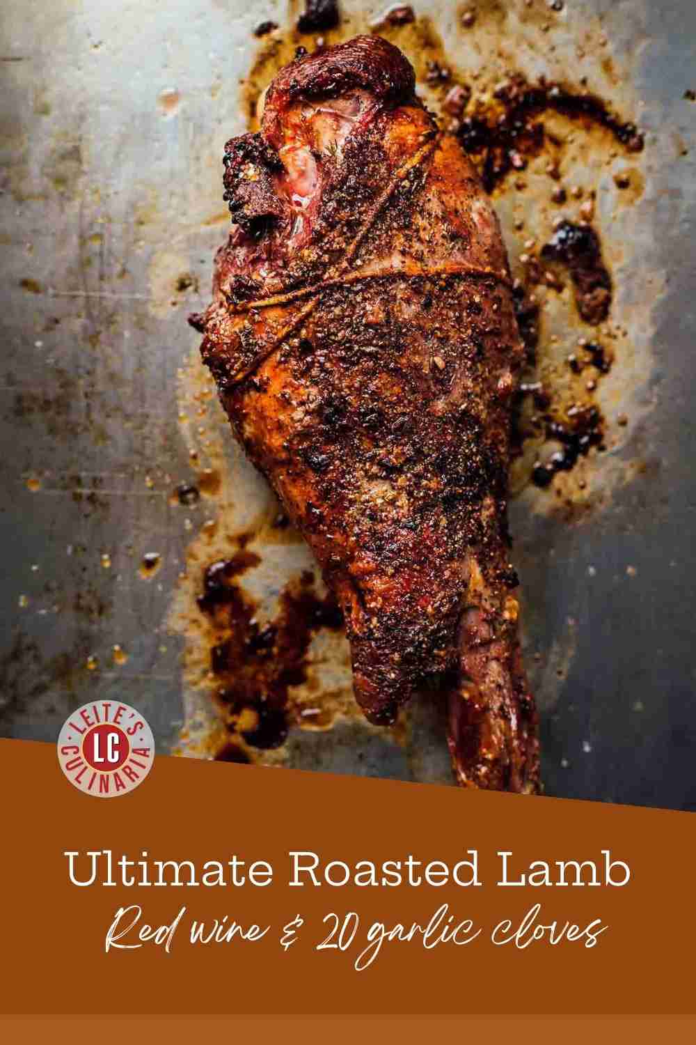 A whole roasted leg of lamb glistening with herb rub and garlic on a rustic metal baking sheet.