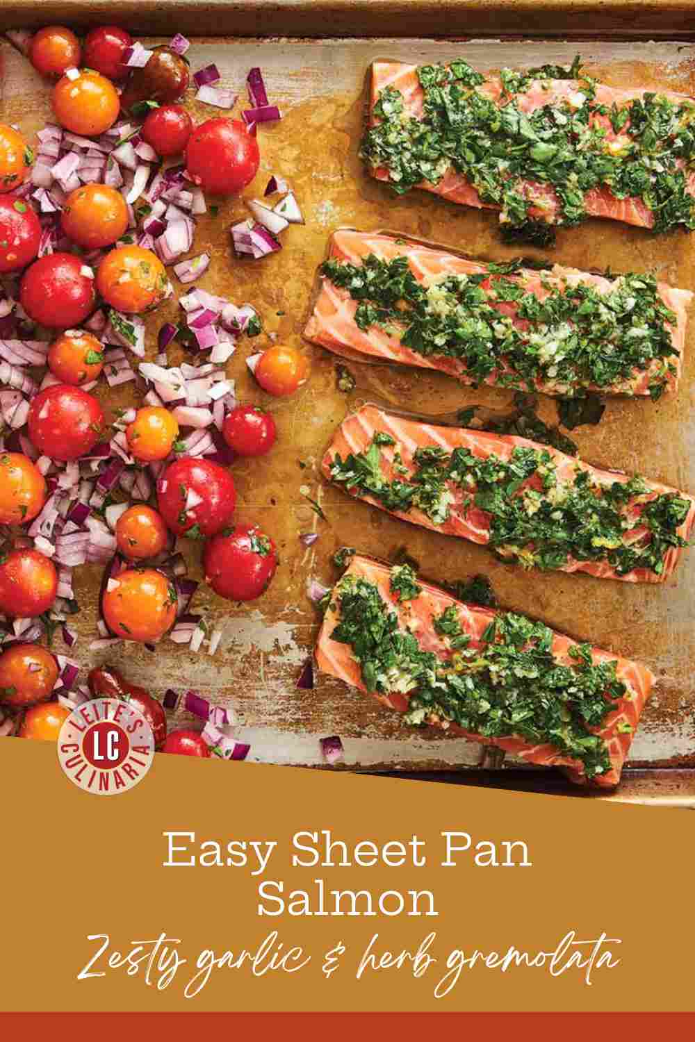 Four salmon fillets topped with green gremolata next to roasted cherry tomatoes and red onions on a baking sheet.