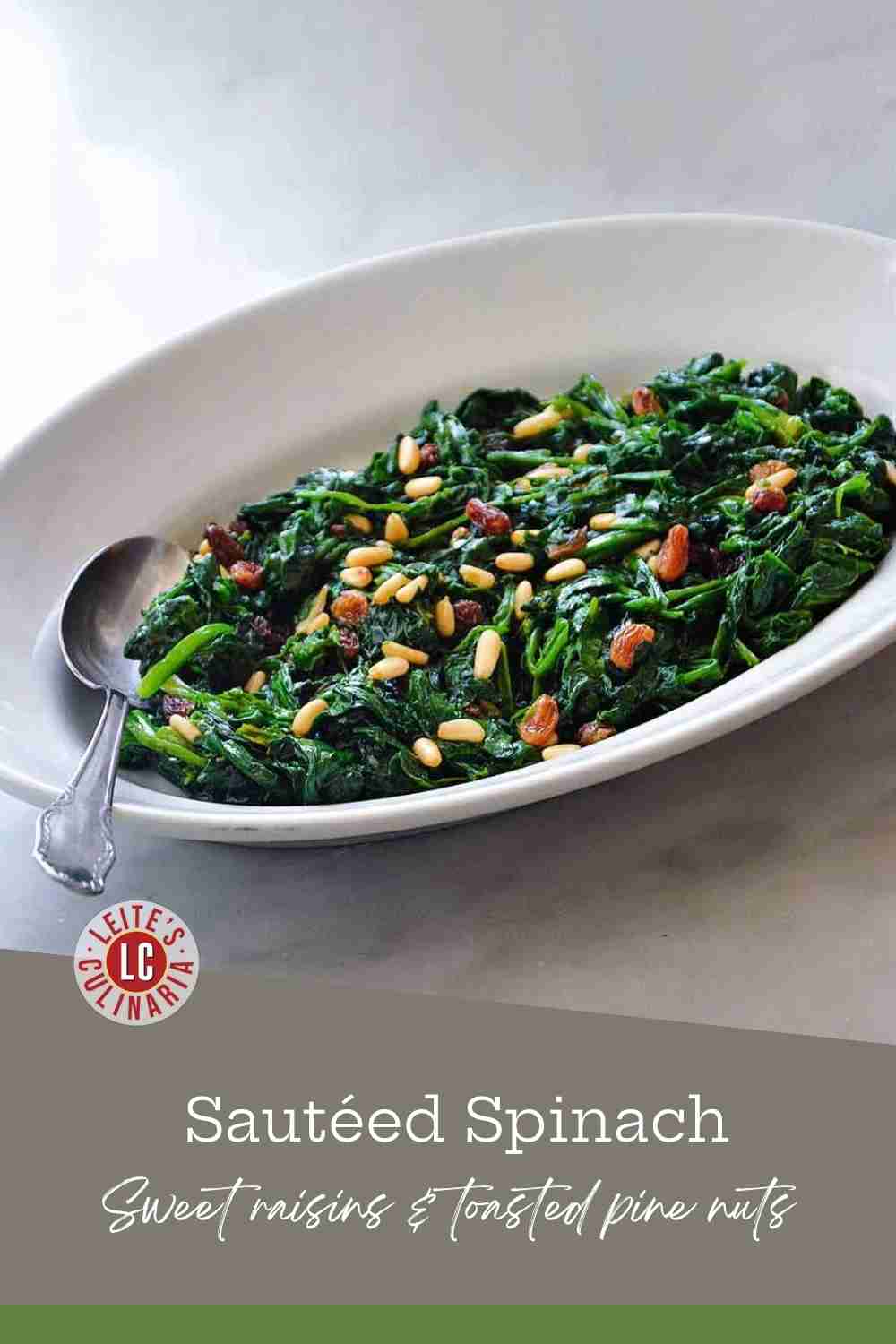 Sautéed green spinach topped with golden pine nuts and raisins in a white oval dish with a silver spoon.
