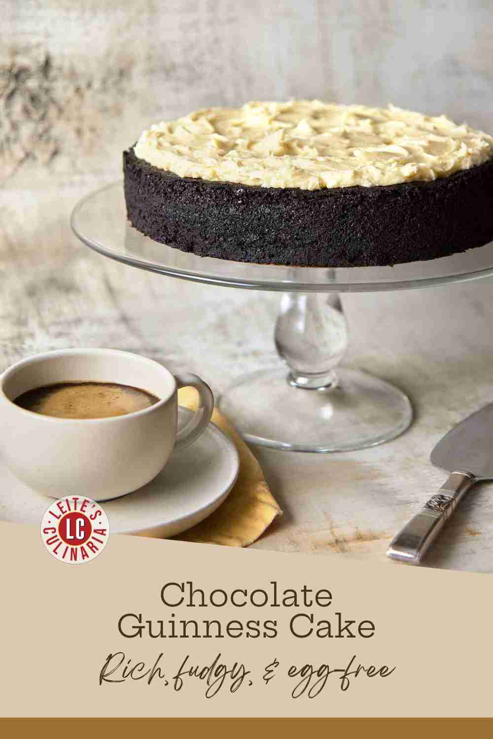A rich, dark chocolate Guinness cake topped with swoops of brown butter cream cheese frosting on a glass cake stand.