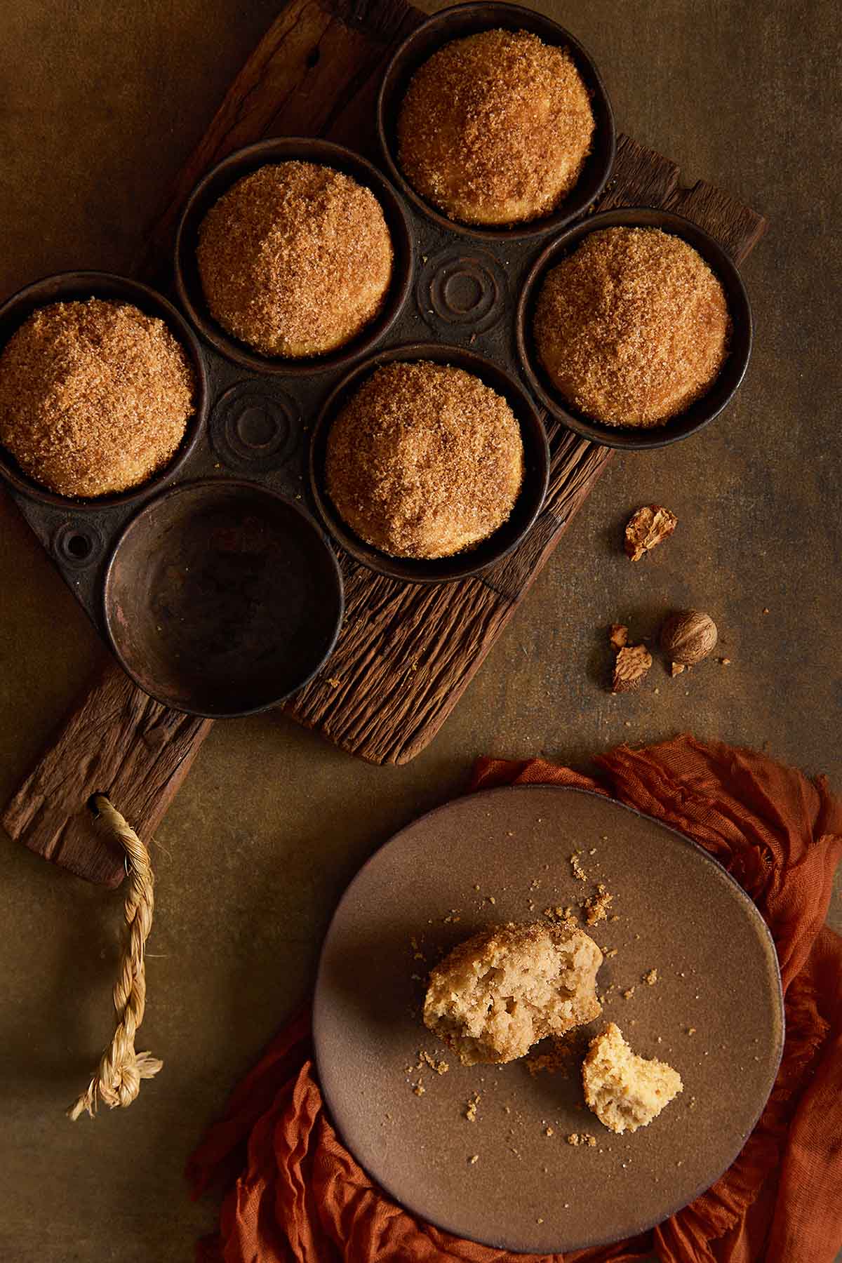 Top-down view of cinnamon sugar muffins in a dark muffin tin next to a halved muffin on a plate.