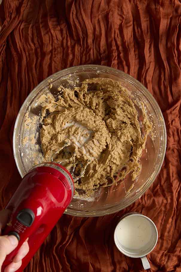 Mixing white milk into the thick muffin batter with a red electric hand mixer.