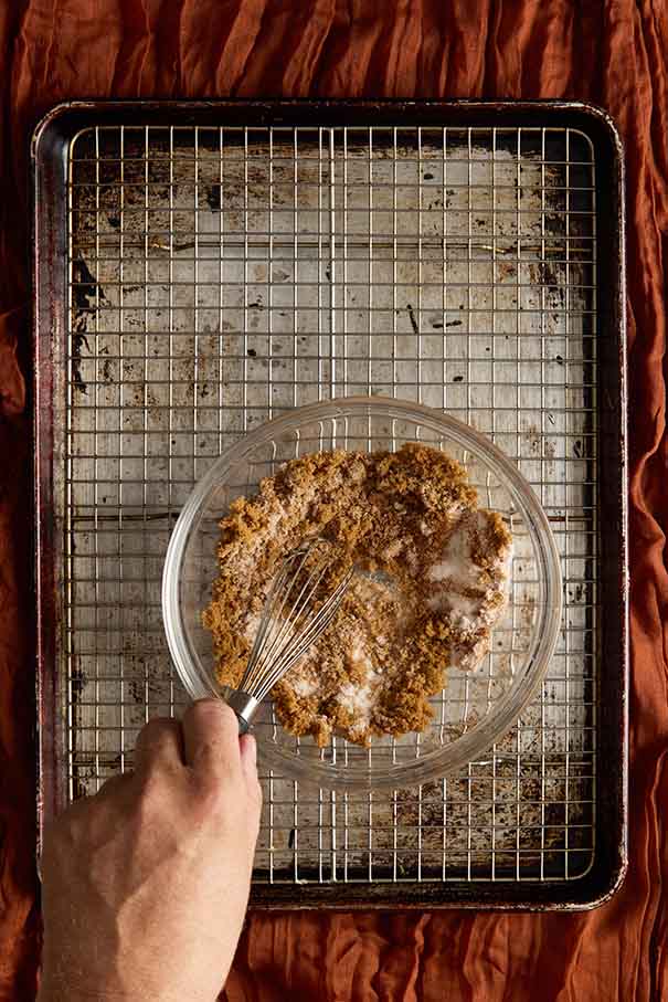 Hand whisking ground cinnamon and granulated sugar in a small bowl on a wire rack.