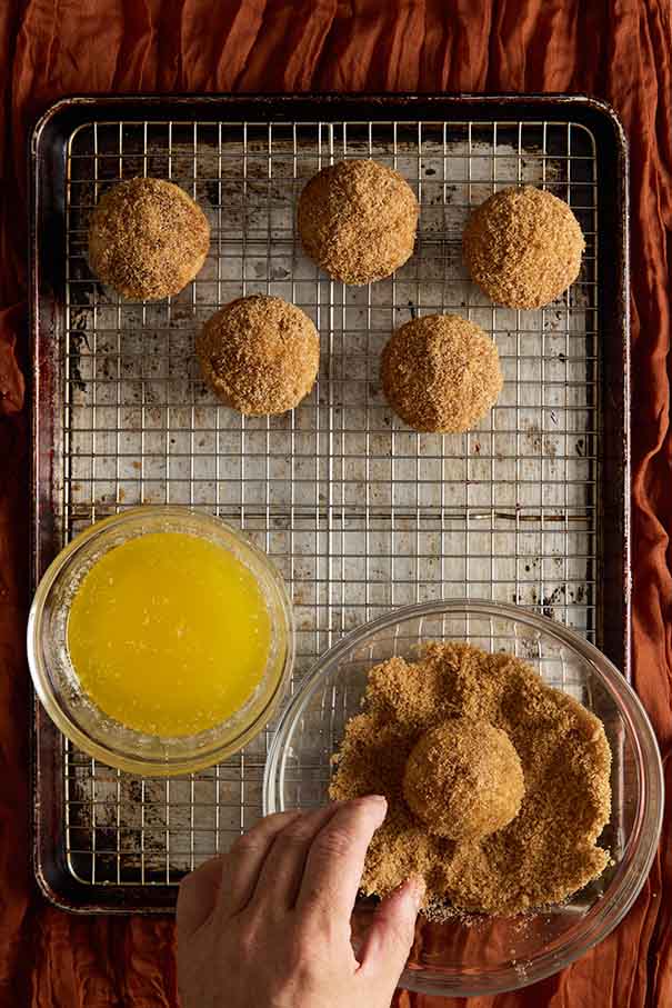 A hand rolling a baked muffin in cinnamon sugar next to a bowl of melted butter.