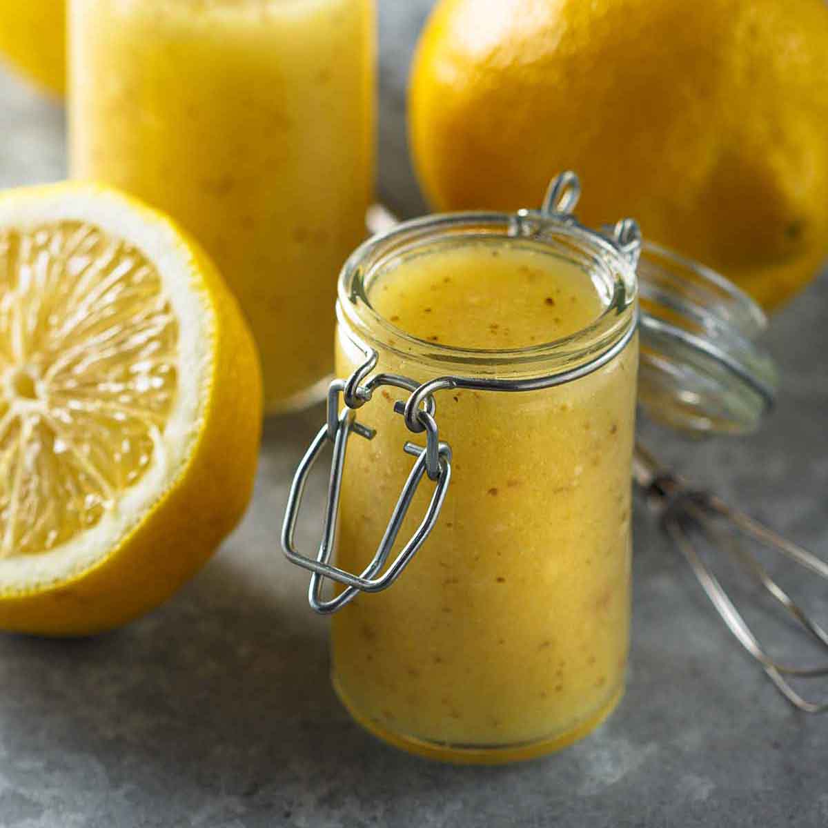 A small jar of lemon vinaigrette with chives, next to sliced lemons.