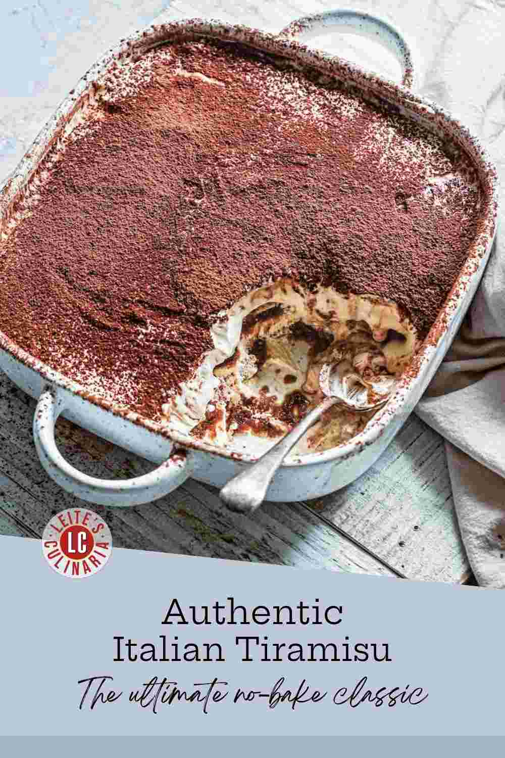 A white ceramic dish holds creamy tiramisu layers topped with a thick dusting of dark cocoa powder.