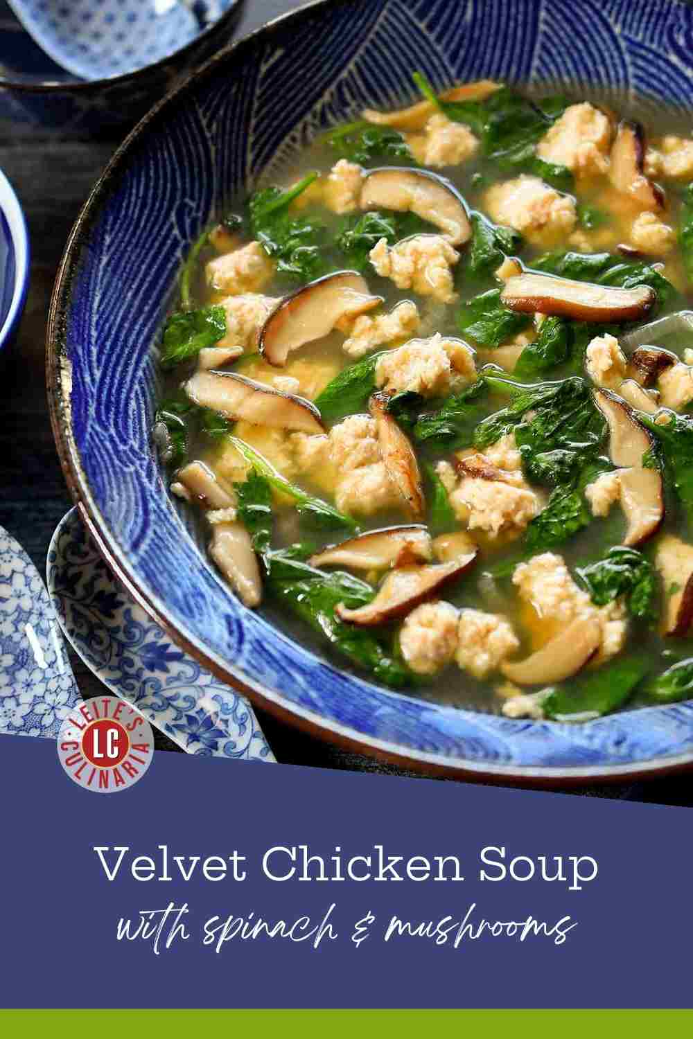 A blue patterned bowl filled with clear broth, tender chicken bits, sliced shiitake mushrooms, and green spinach.