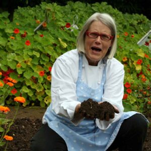 The Irish cookbook author and teacher, Darina Allen, crouching in a garden.