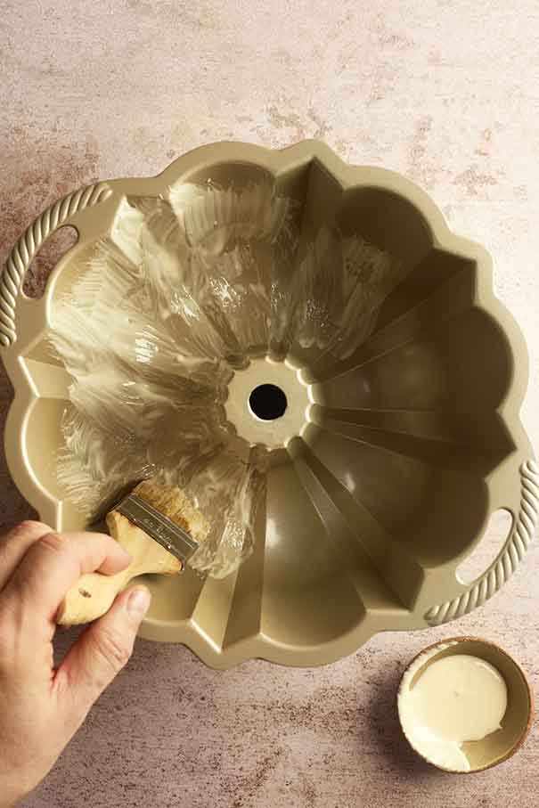 A hand uses a brush to coat the inside of a gold Bundt pan with Cake Goop.