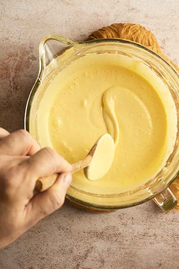 Cake batter falling from a wooden spoon in a thick ribbon to show eggs and sugar are combined.