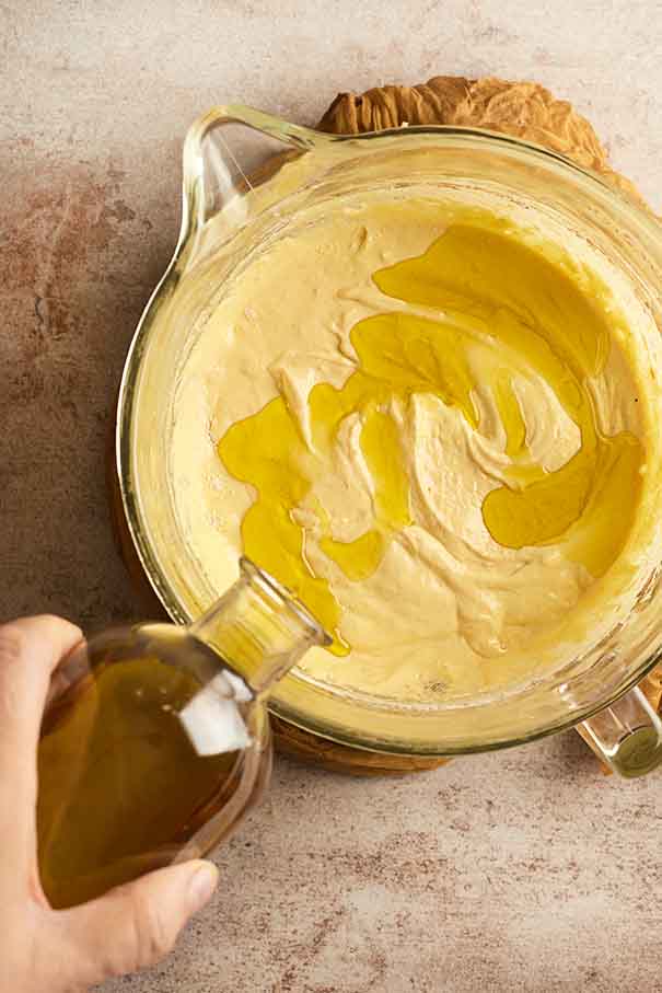 Extra virgin olive oil being slowly drizzled from a glass bottle into the cake batter.