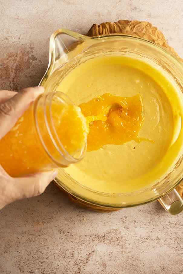 Freshly squeezed orange juice being poured into golden cake batter for moisture and citrus flavor.