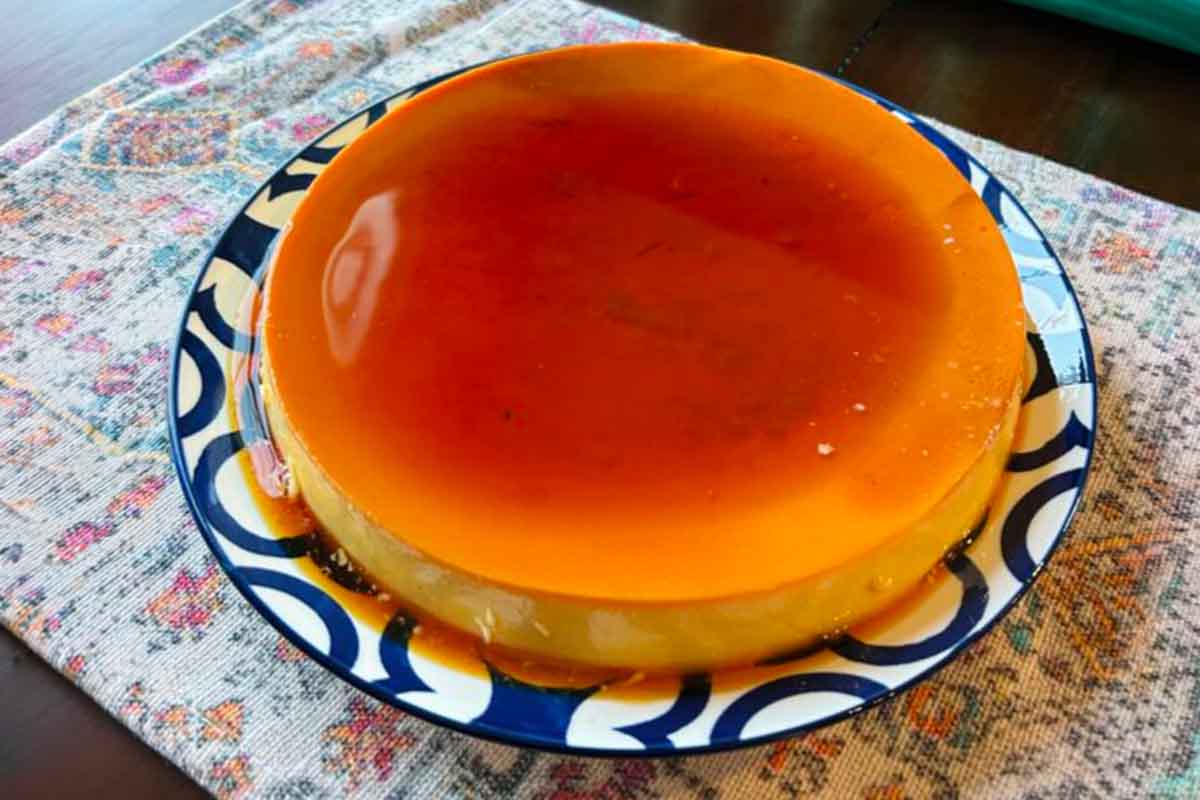 A perfect amber-gold round Spanish flan on a blue and white plate on a flowered table mat.