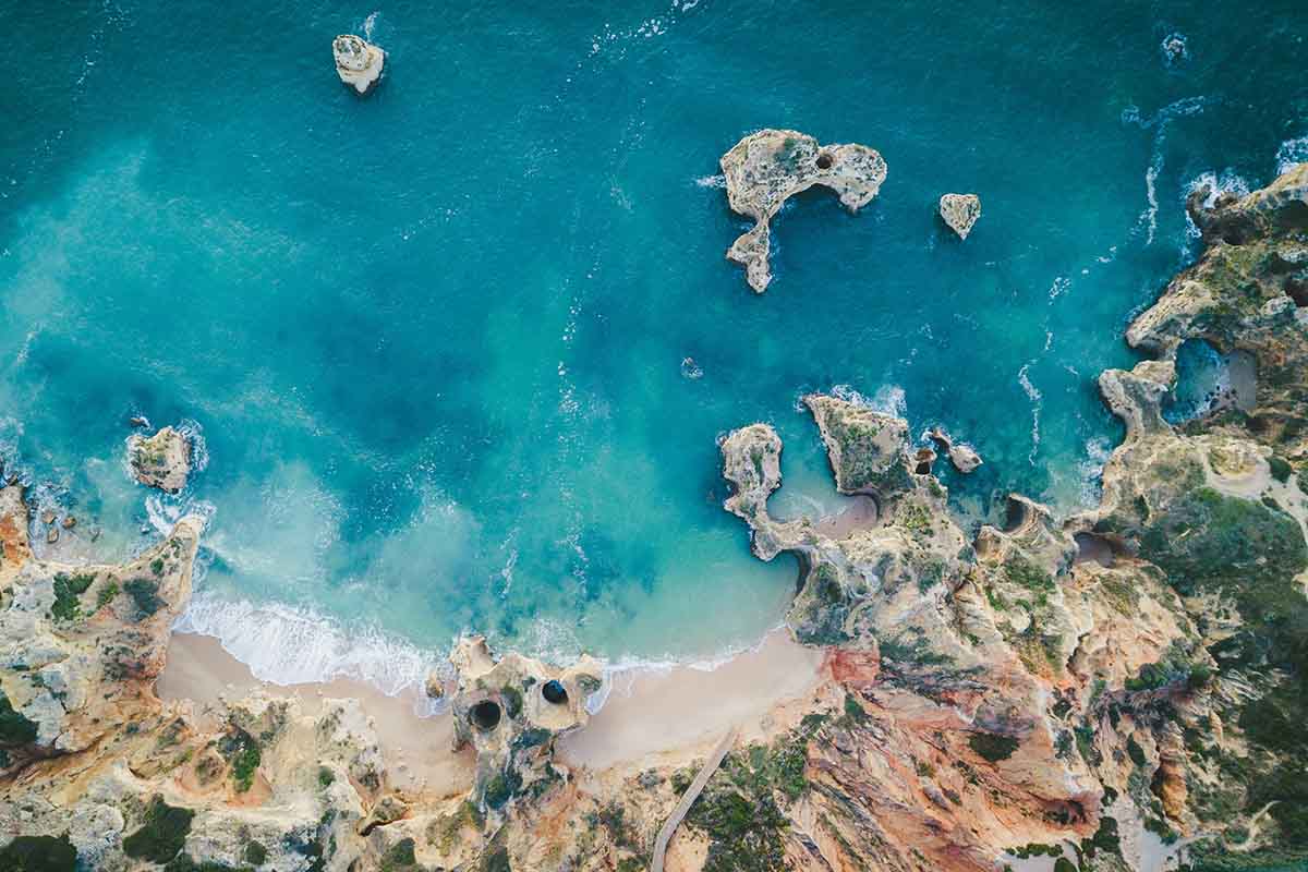 An arial short of the Algarve coast with pristine blue waters and sandy and craggy beaches.