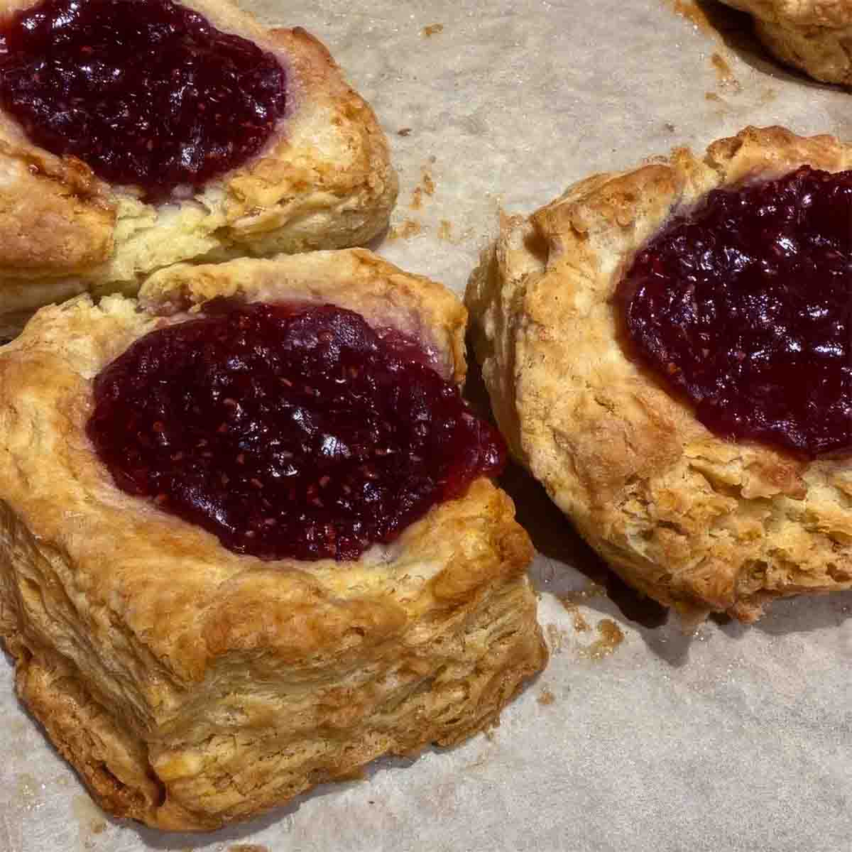 Three biscuits baked with dollops of raspberry jam on top.
