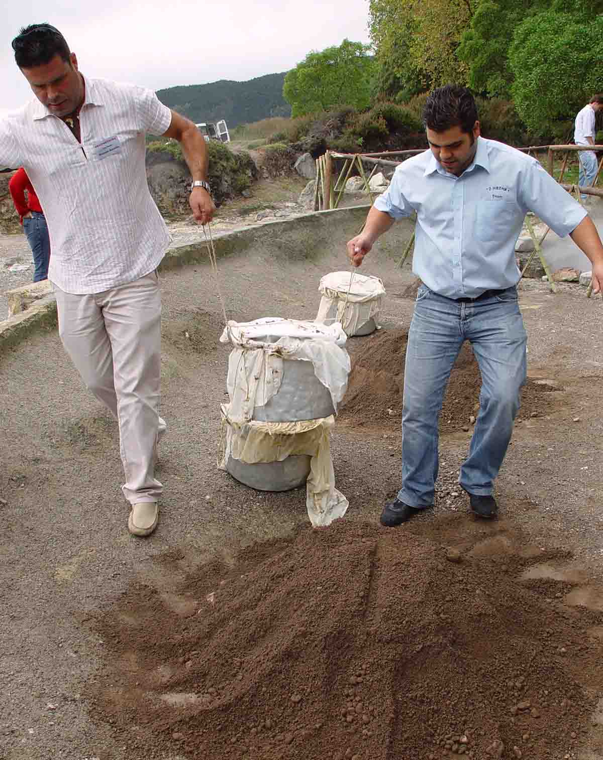 Two men lifting a cloth-wrapped pot of food that has been cooking in a volcanic fissure for hours.