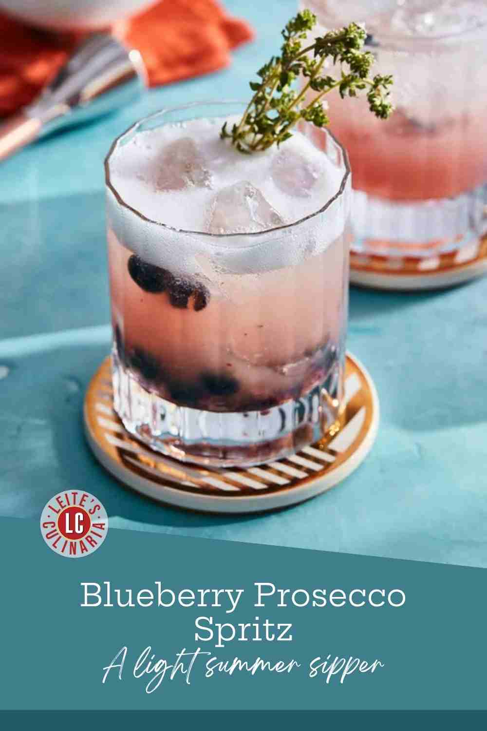 A tall glass of blueberry Prosecco spritz over ice with a thyme sprig, on a teal surface.