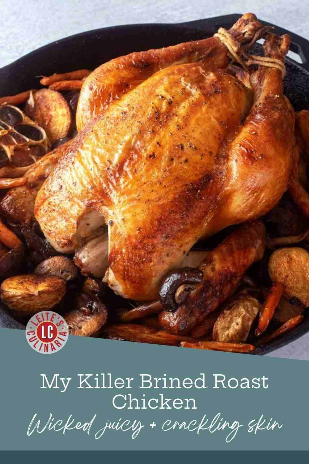 A whole roast chicken with deep golden skin in a cast-iron skillet, surrounded by potatoes, carrots and mushrooms.