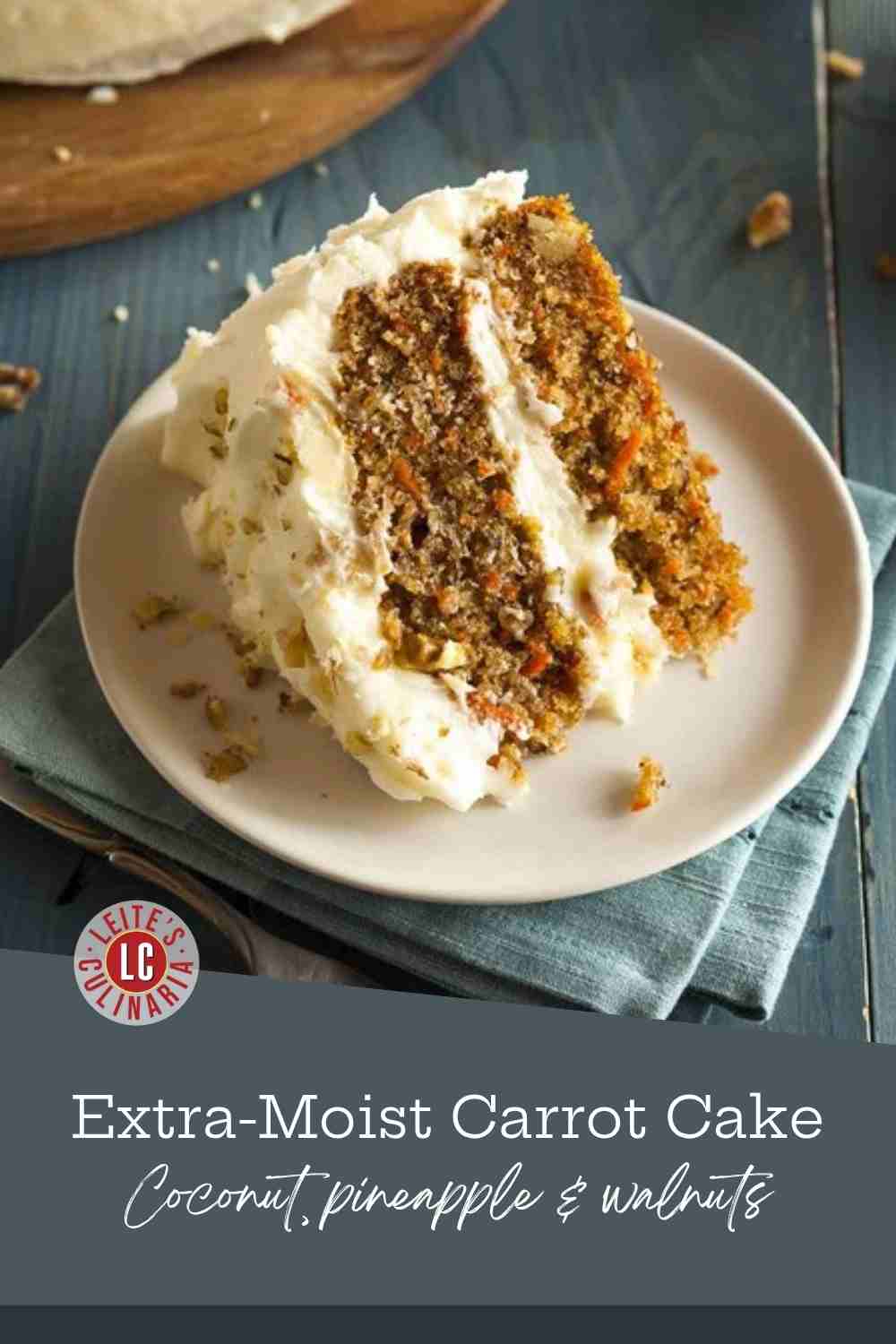 A slice of layered carrot cake with thick cream cheese frosting on a plate, the whole cake behind it.