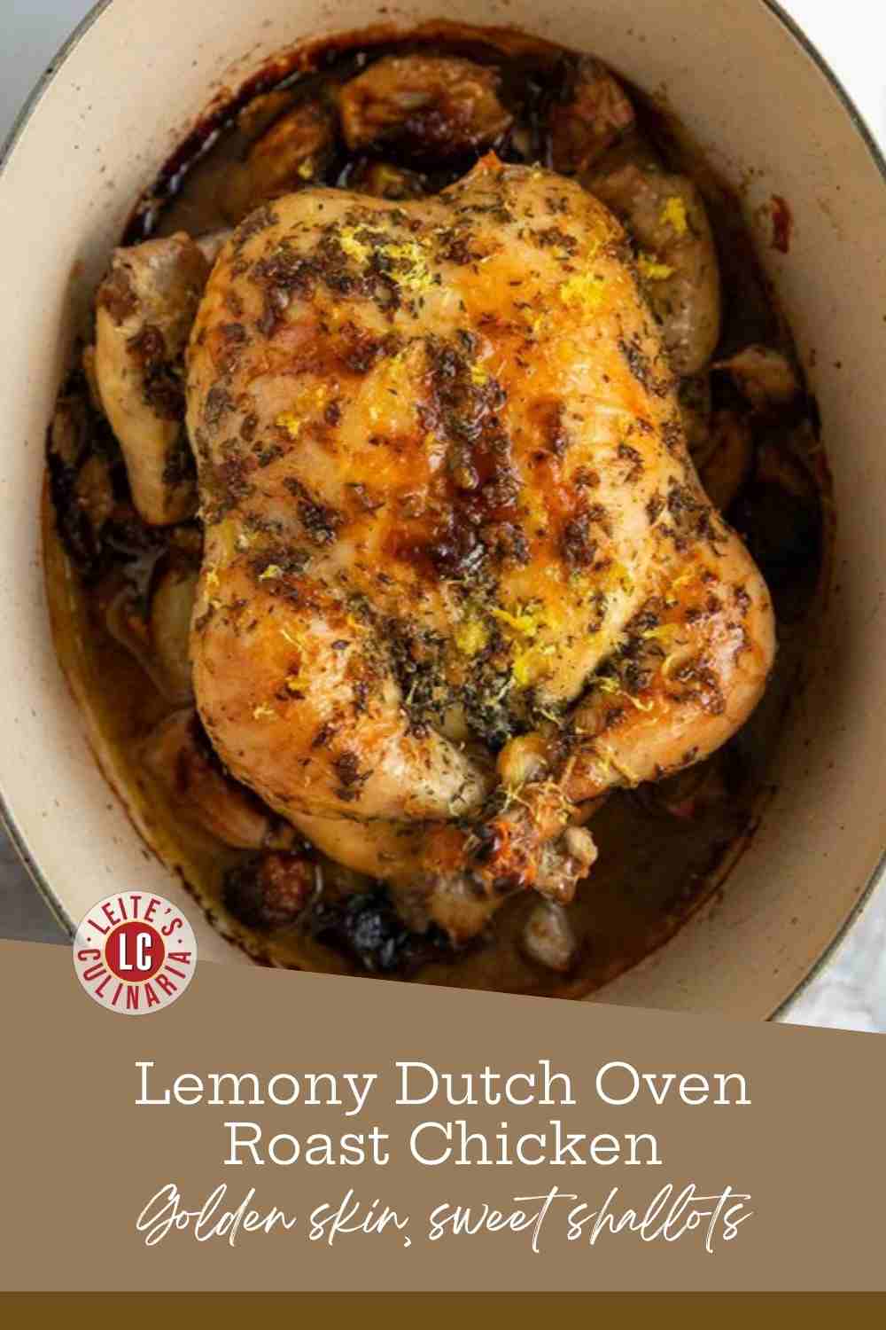 A whole roast chicken with crisp golden skin nestled among shallots and garlic in a Dutch oven.