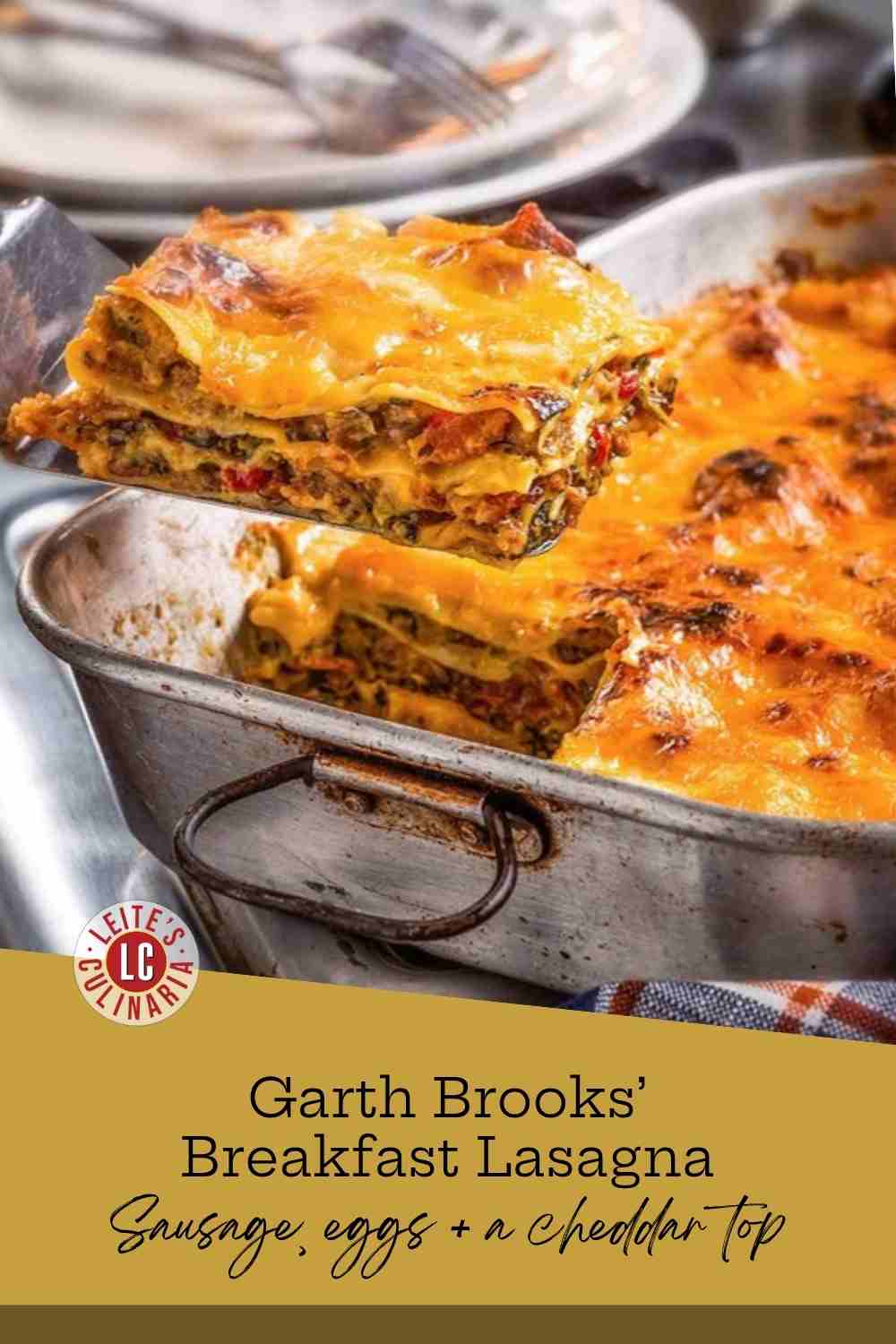 A metal spatula lifting a square of breakfast lasagna from a battered sheet pan, cheddar melting at the edges.