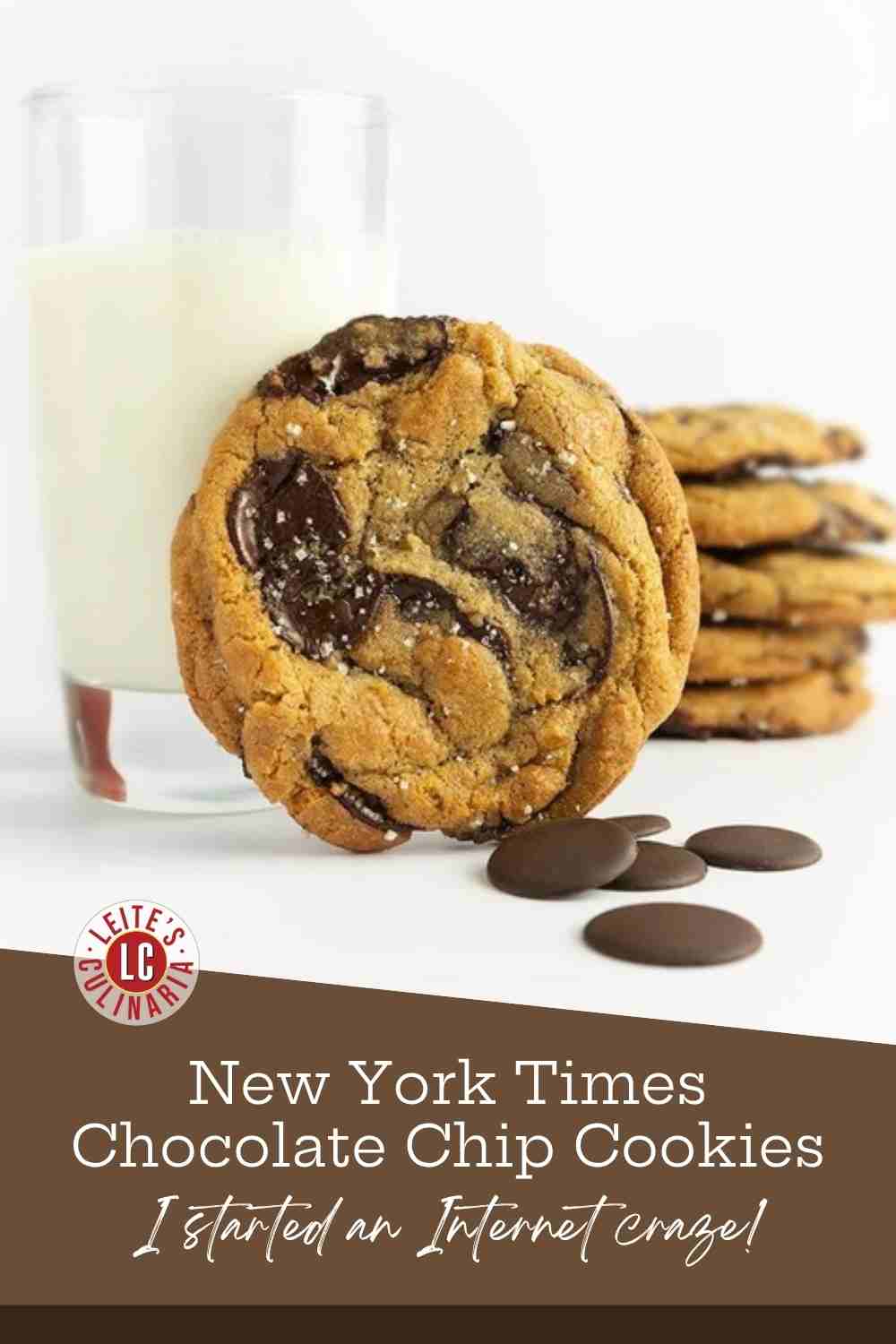 Chocolate chip cookies stacked beside a glass of milk with bittersweet chocolate discs scattered around.