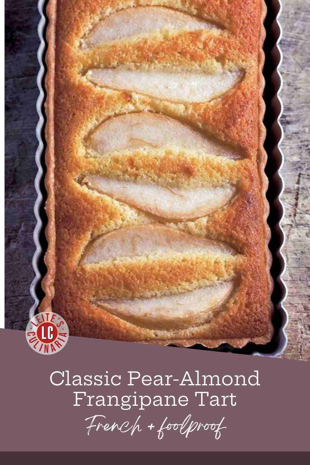 Fanned pear halves baked into golden frangipane in a fluted tart pan on weathered wood.