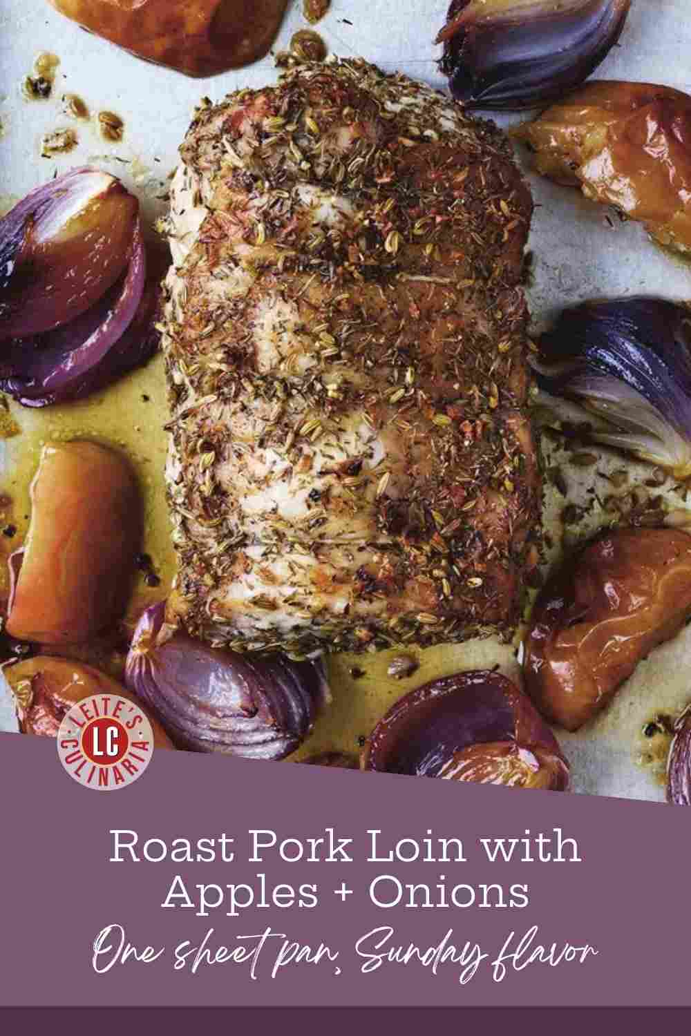 An herb-crusted pork loin on a sheet pan, ringed with red onion wedges and golden apples in the pan juices.