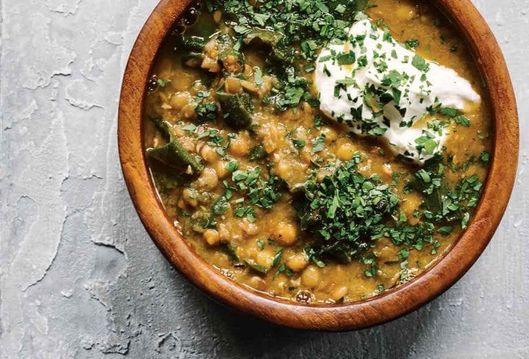A wooden bowl filled with lentil soup with kale, topped with parsley and sour cream.