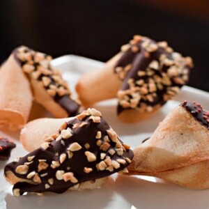 Five change your fortune cookies, coated with chocolate and nuts on a white platter.