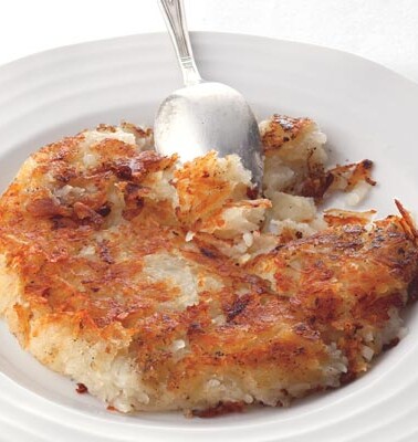 A cooked crisp potato cake on a white plate with a spoon resting in the potato cake.