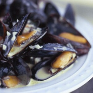 A white plate topped with curried steamed mussels in a creamy sauce.