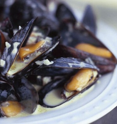 A white plate topped with curried steamed mussels in a creamy sauce.