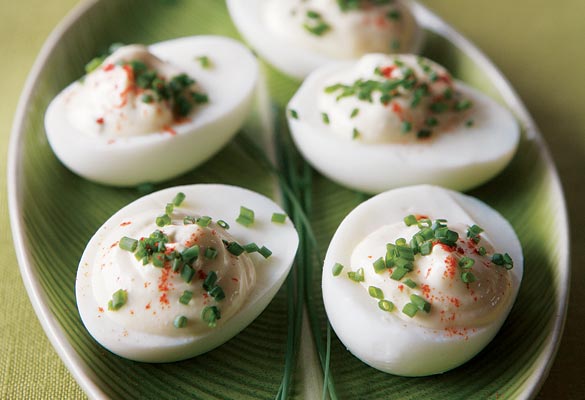 Five low-fat deviled eggs on a leaf shaped plate, garnished with a sprinkle of chives and paprika