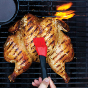 A spatchcocked and grilled Five-Spice chicken on a barbecue being brushed with marinade.