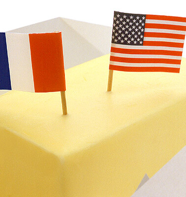 A stick of butter unwrapped with a small paper French flag and a small paper American flag both stuck in it.