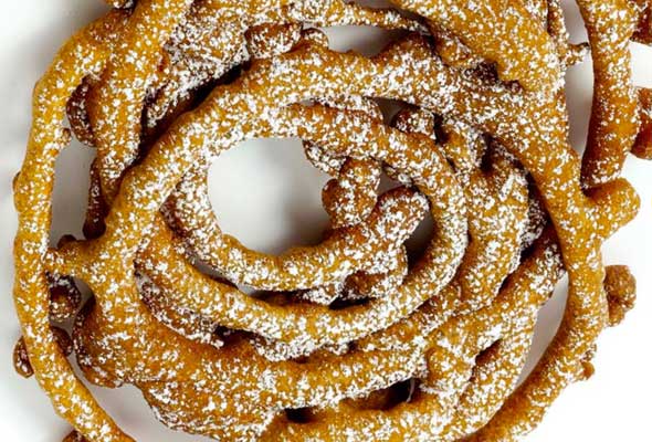 A pile of funnel cakes on a plate, all dusted with icing sugar.
