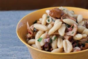 Gnocchetti with pancetta, chanterelles, and mint piled in a yellow bowl on a blue linen tablecloth.