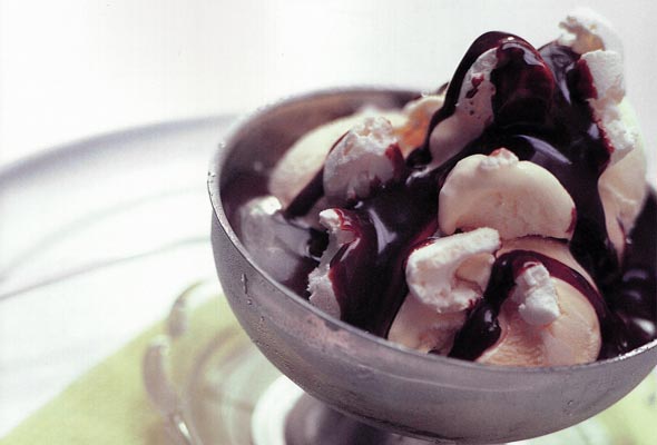 Hot chocolate sauce drizzled over scoops of vanilla ice cream and chopped nuts in a metal bowl.