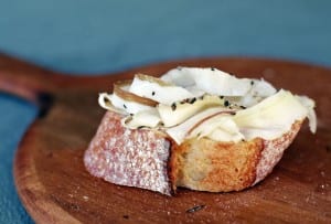 A slice of rustic bread topped with thin slices of lardo, all on a wooden cutting board