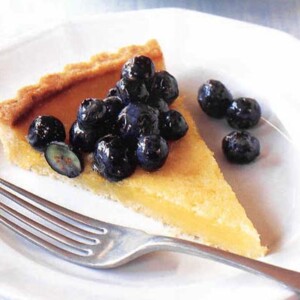 A slice of lemon tart with blueberries on a white plate with a fork.