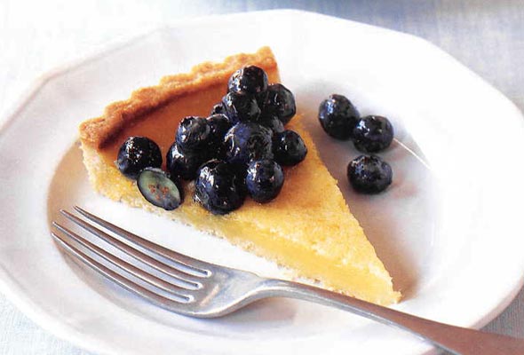 A slice of lemon tart with blueberries on a white plate with a fork.