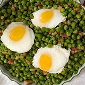 Portuguese Peas and Eggs in a white scalloped bowl with a silver serving spoon.