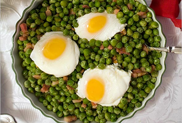 Portuguese Peas and Eggs in a white scalloped bowl with a silver serving spoon.