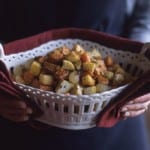 A person holding a basket of roasted caramelized root vegetables.